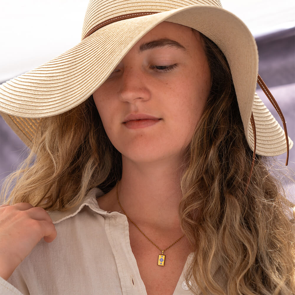 Woman wearing a wide-brimmed hat with a blurred background wearing a gold GAIA rectangular necklace