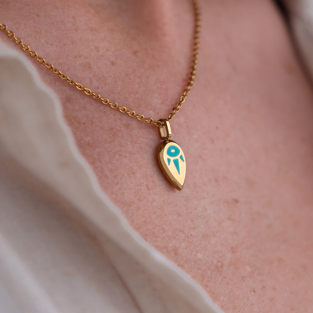 Gold SERENE necklace with a blue pendant on a person's neck