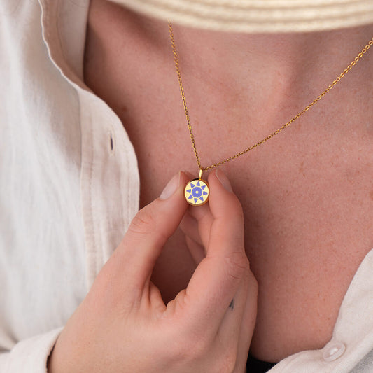 Gold necklace with a purple and gold SOLIS pendant held by a hand against a neutral background