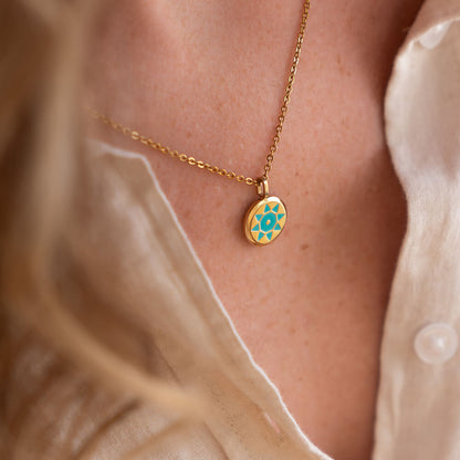 Gold SOLIS necklace with a gold and blue pendant on a person wearing a beige top.